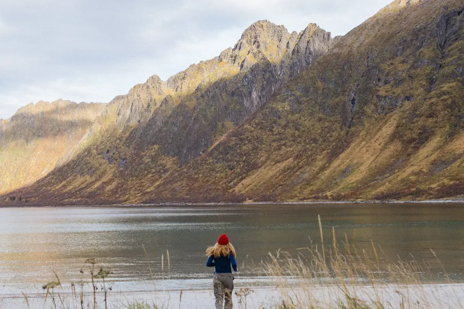 Person med rød lue ser ut over en fjord med fjell i bakgrunnen